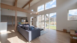 A spacious living area with a large gray sofa, wooden beams, and large windows offering a view of the outdoors. - Country Resort Niseko (Kutchan)