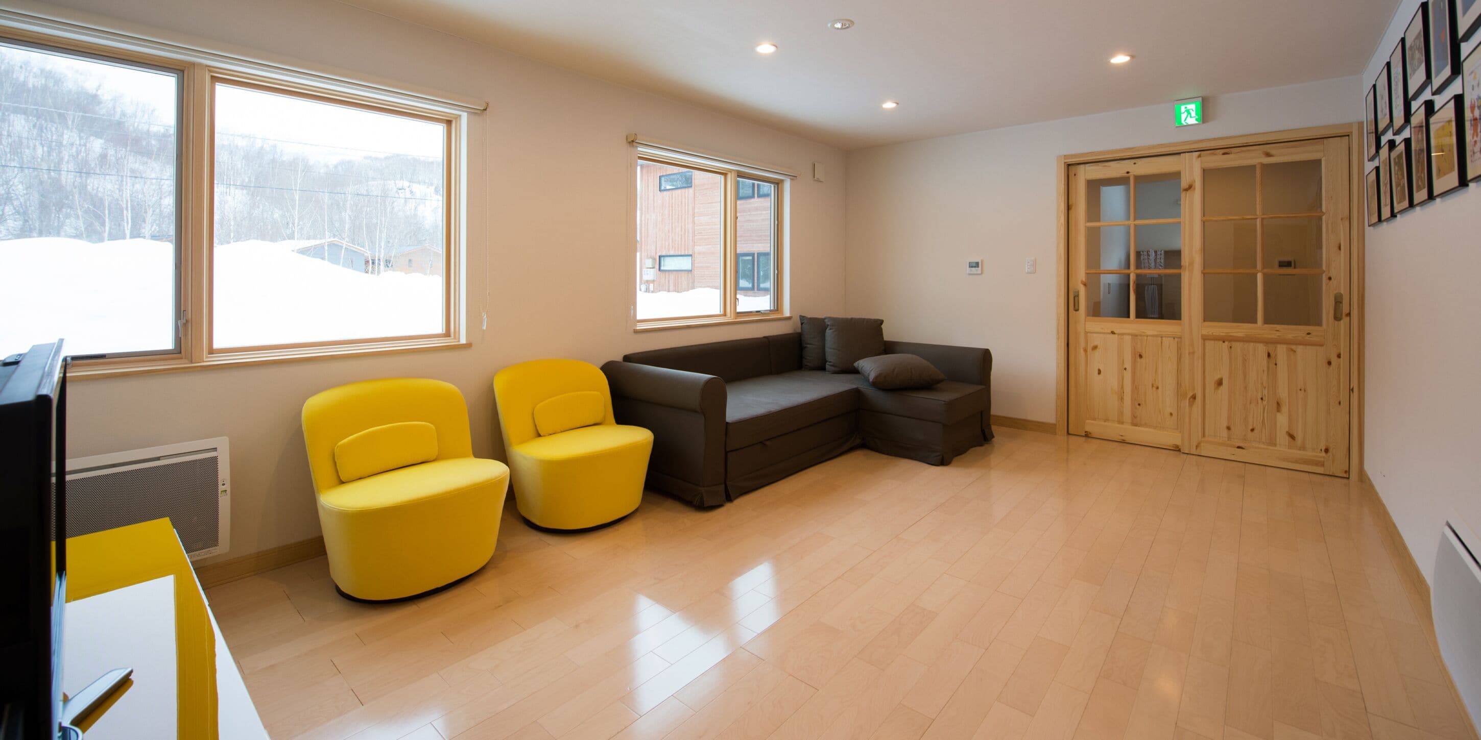 A room with a wooden floor, two yellow chairs, a brown sofa, and a wooden cabinet with glass doors.