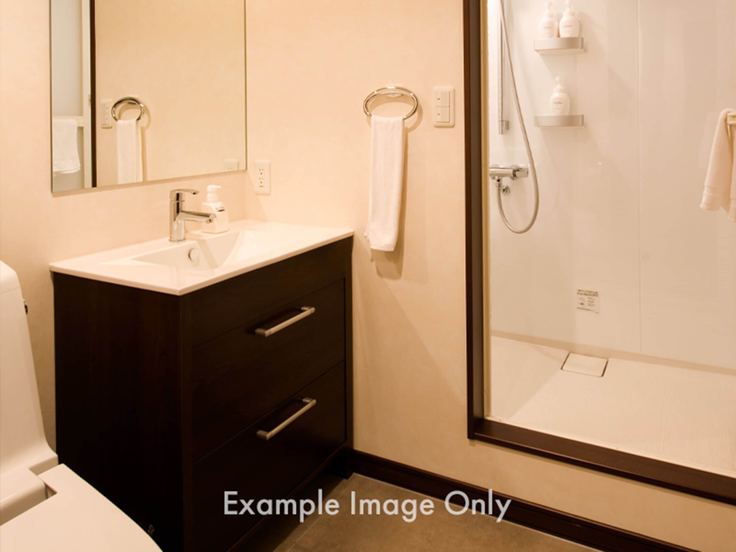 A bathroom with a sink, mirror, dark cabinet, and a glass shower enclosure.