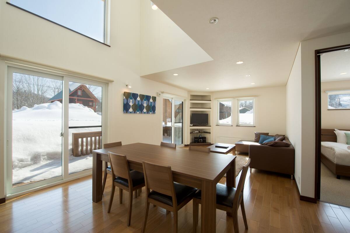 A modern interior with a wooden dining table and chairs, a sofa, and a bed.