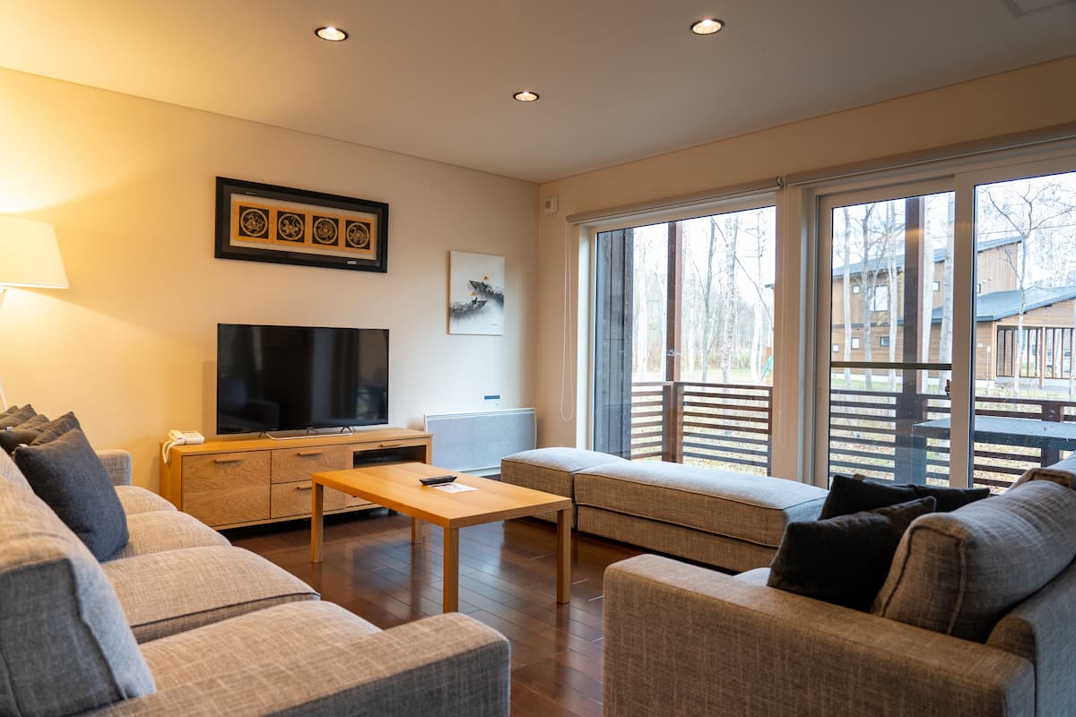 A modern living room with a sofa, a coffee table, a TV, and a large window with a view of the outside.