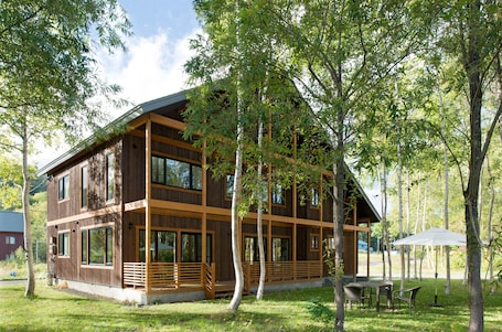 A two-story wooden cabin with large windows, a wooden deck, and a dining area with outdoor furniture.