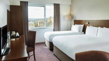 A hotel room with a bed, a desk, a chair, a TV, and a window with a city view.
