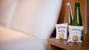 A wooden bedside table with two bottles and two packets of snacks.