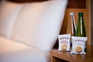 A wooden bedside table with two bottles and two packets of snacks.
