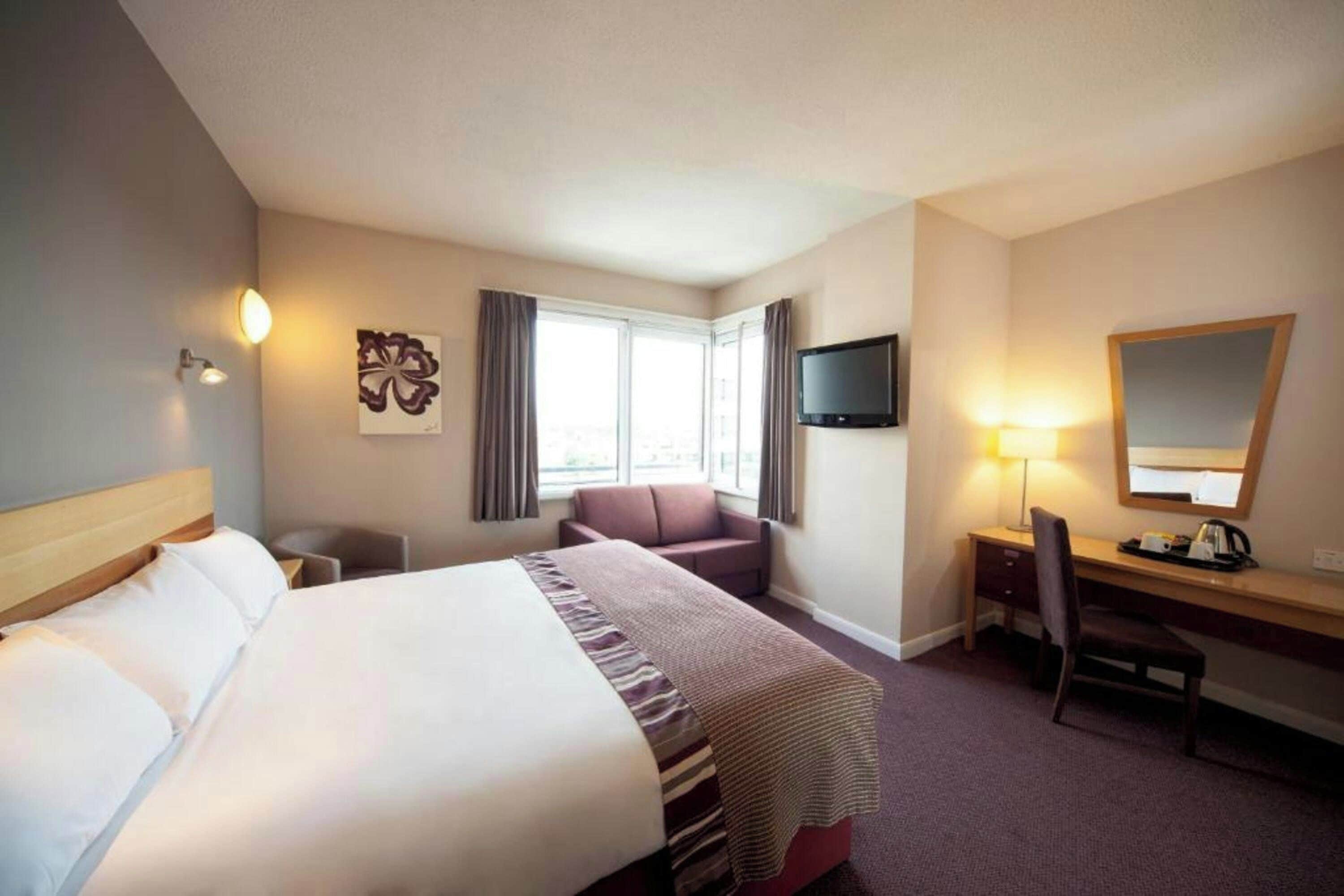 A hotel room with a bed, a desk, a chair, a television, and a window with curtains.