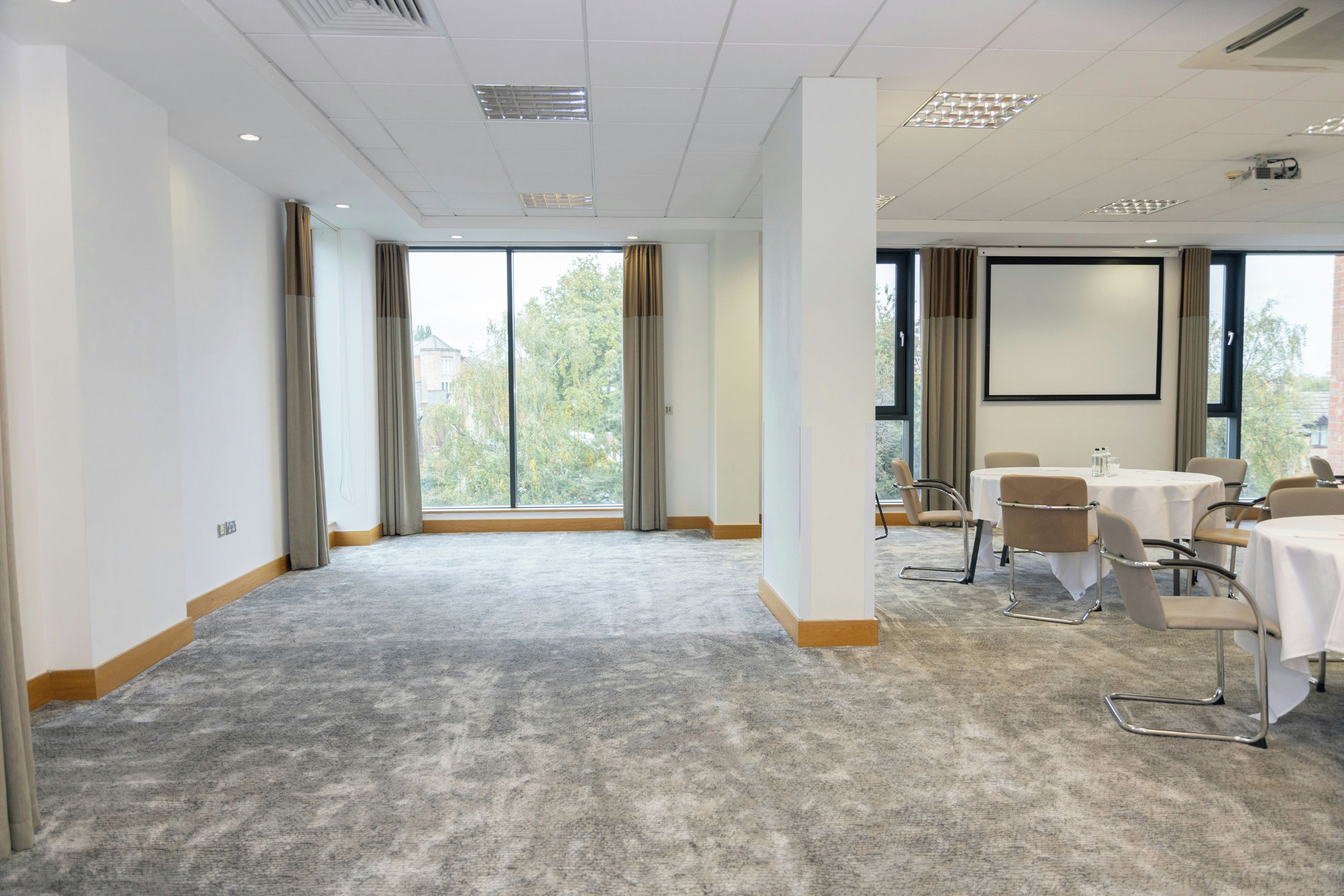 A conference room with a large window, carpeted floor, and a projector screen.