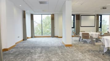 A conference room with a large window, carpeted floor, and a projector screen.