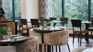 A restaurant interior with round tables, chairs, and a view of greenery through large windows.