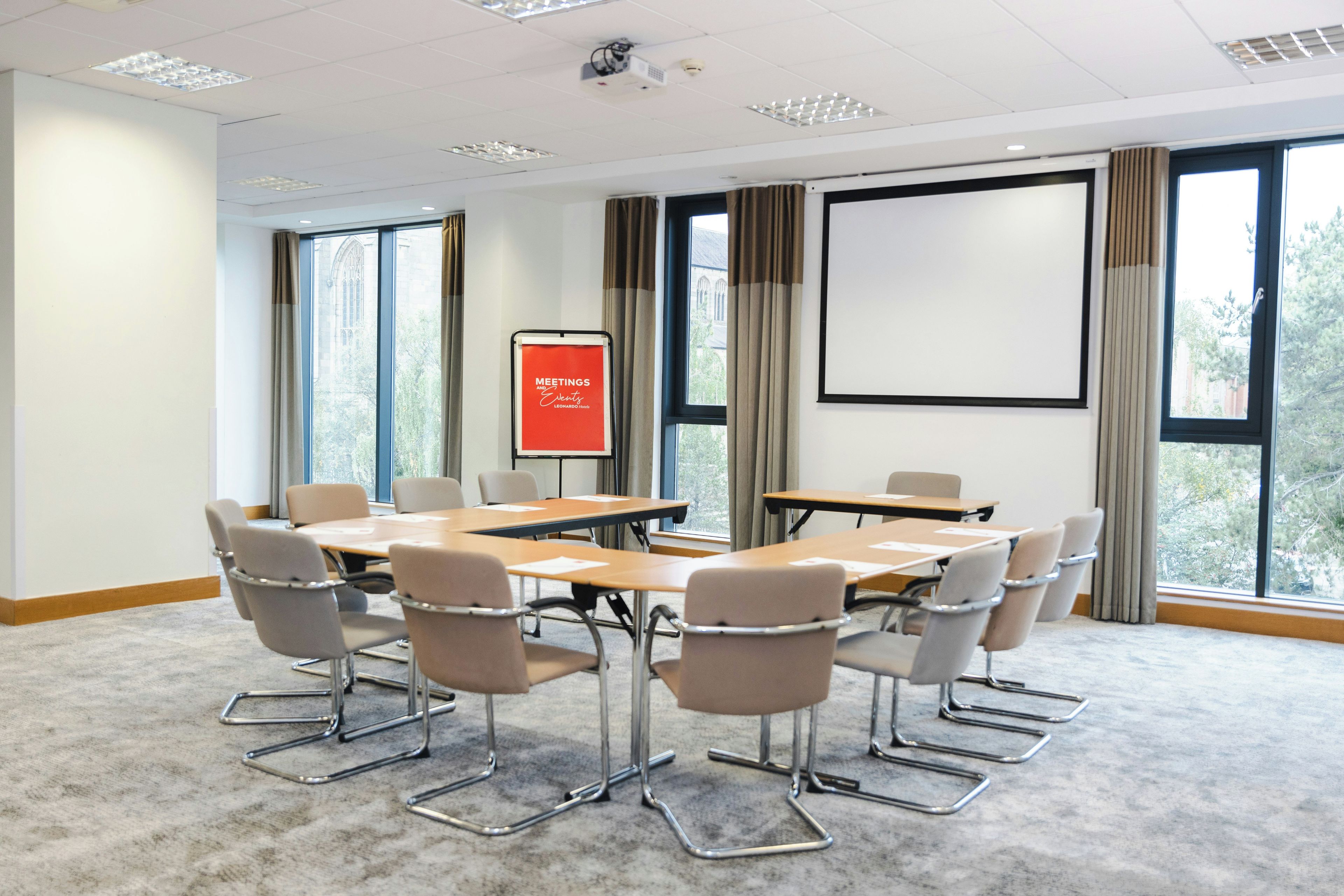 A conference room with a large table, chairs, a projector screen, and large windows.