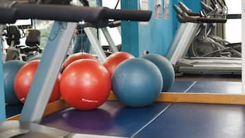 Equipo de ejercicio que incluye cintas de correr y pelotas de gimnasia en un entorno de gimnasio.
