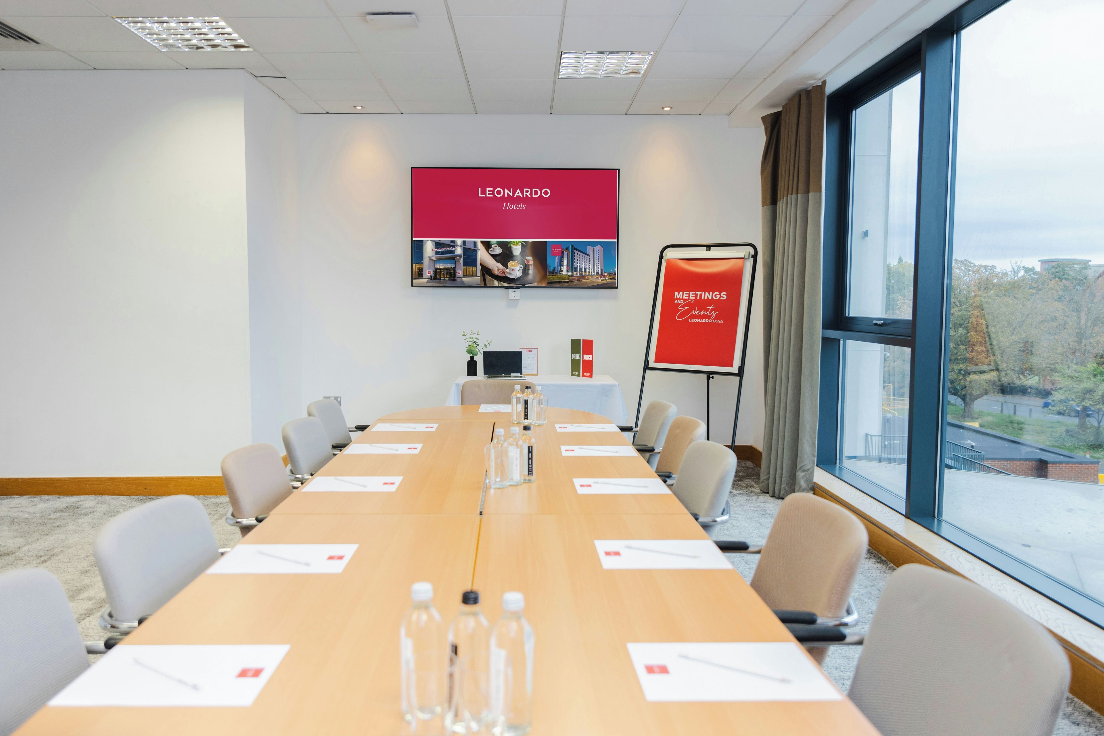 A conference room with a long table, chairs, a projector screen, and a view of the outdoors.
