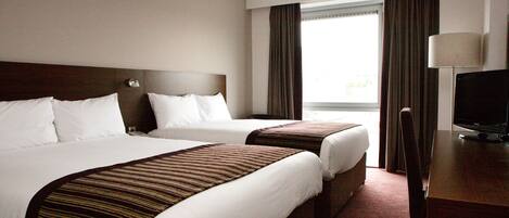 A hotel room with two beds, a desk with a lamp, and a television.