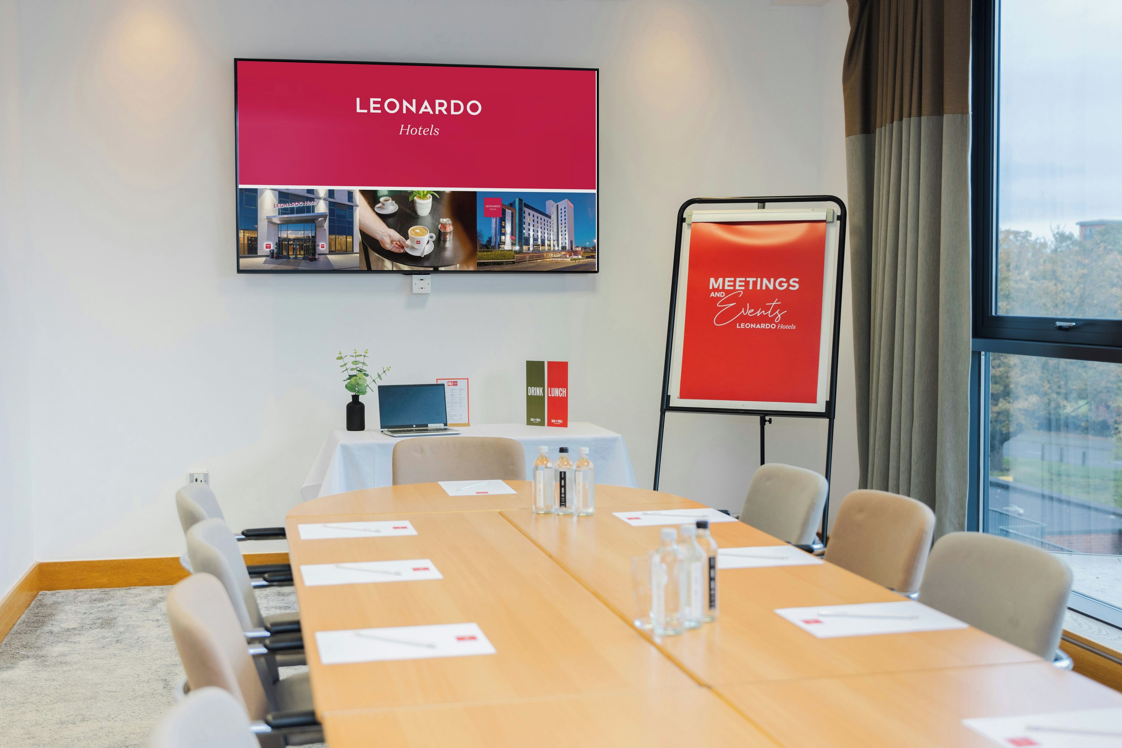 A conference room with a long table, chairs, a laptop, a projector screen, and a banner.