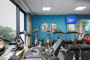 A gym with various cardio machines, a television displaying workout routines, and exercise posters on the wall. - Leonardo Hotel Derby (Derby)
