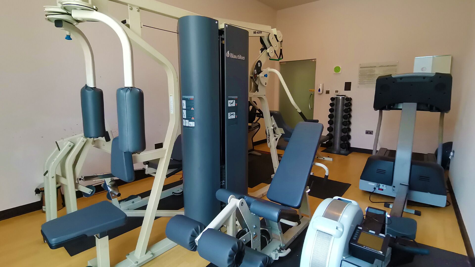 A gym with various exercise equipment including weight machines, a bench, and dumbbells.
