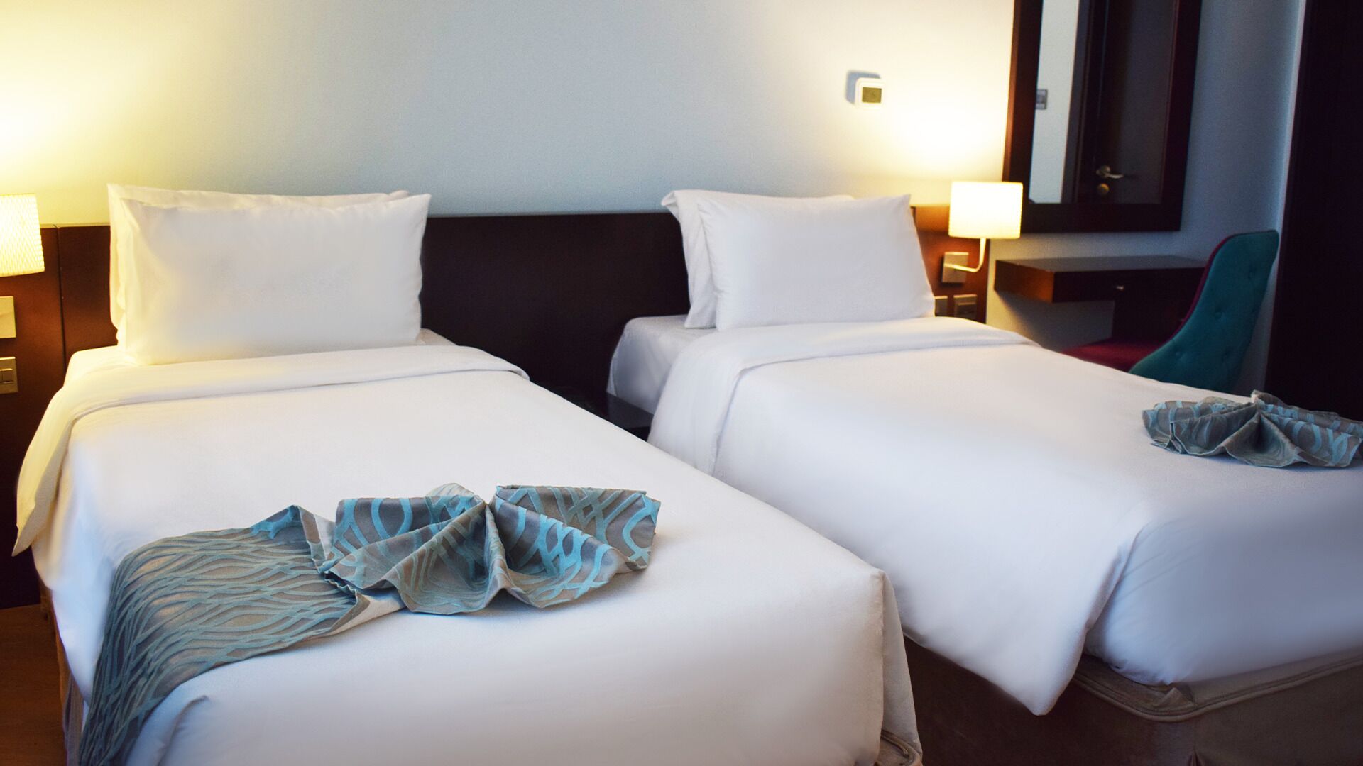 A hotel room with two single beds, white bedding, and a blue patterned throw on the left bed.