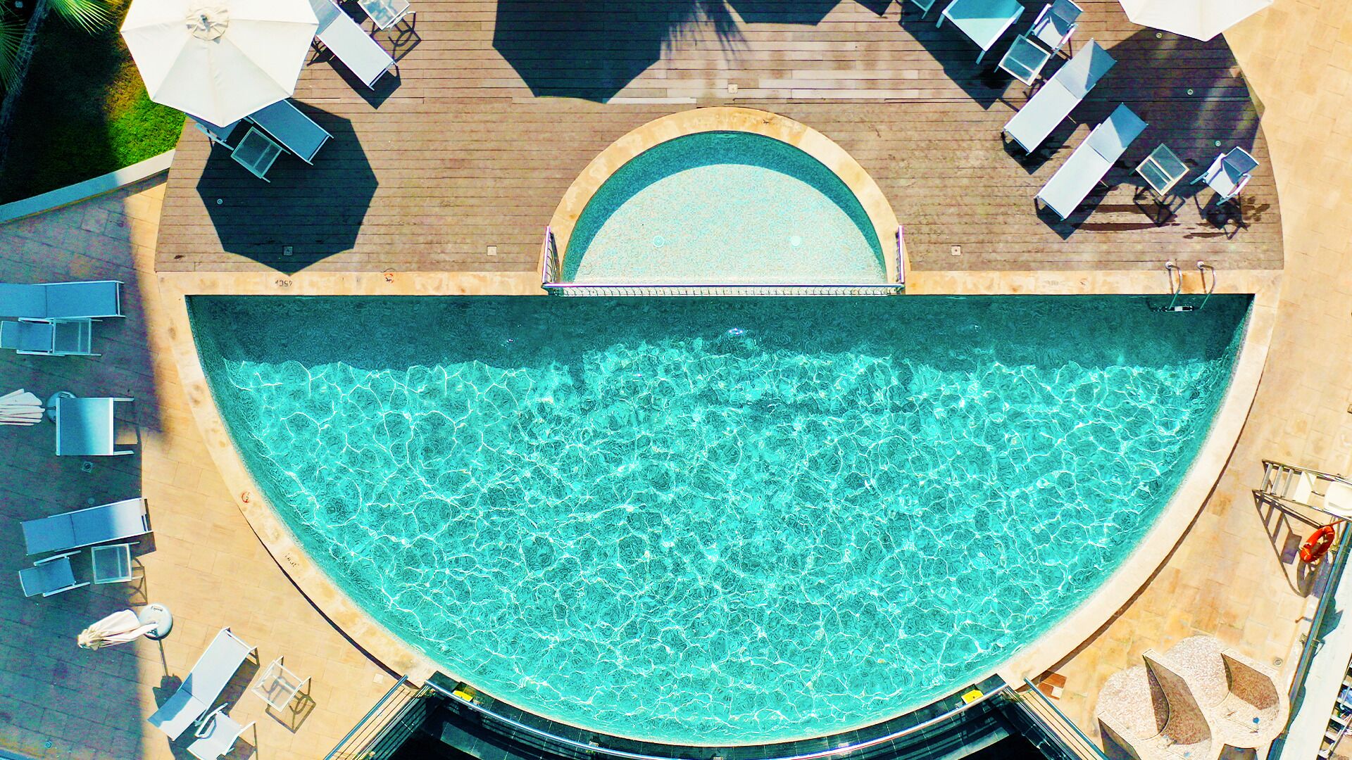 An aerial view of a pool area with a curved edge, surrounded by lounge chairs and umbrellas.