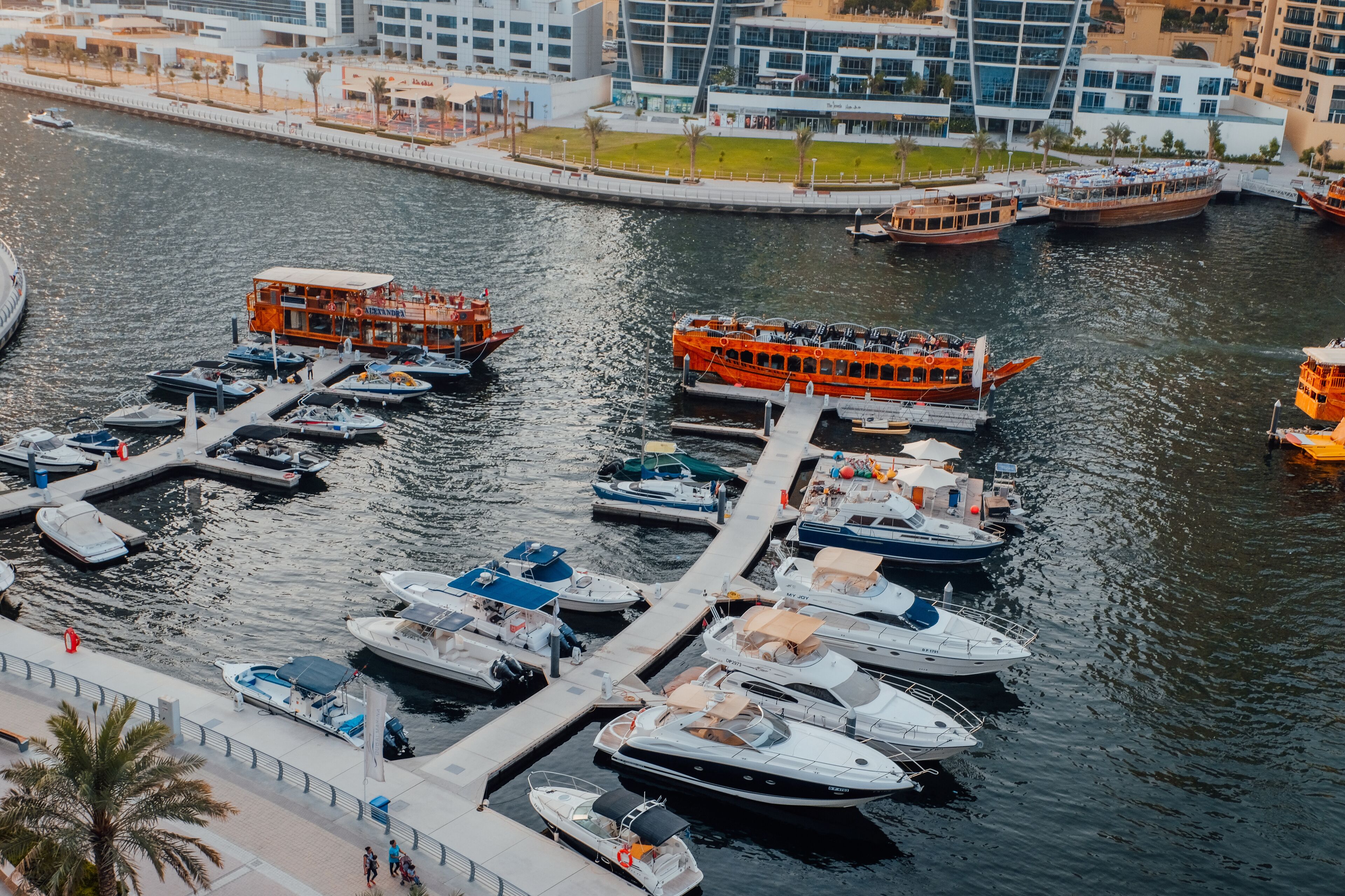 A marina with various boats docked at a pier, surrounded by modern buildings.