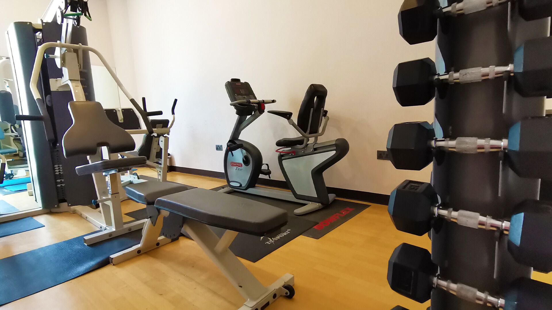 A gym with exercise equipment including a bench press, a stationary bike, and a rack of dumbbells.