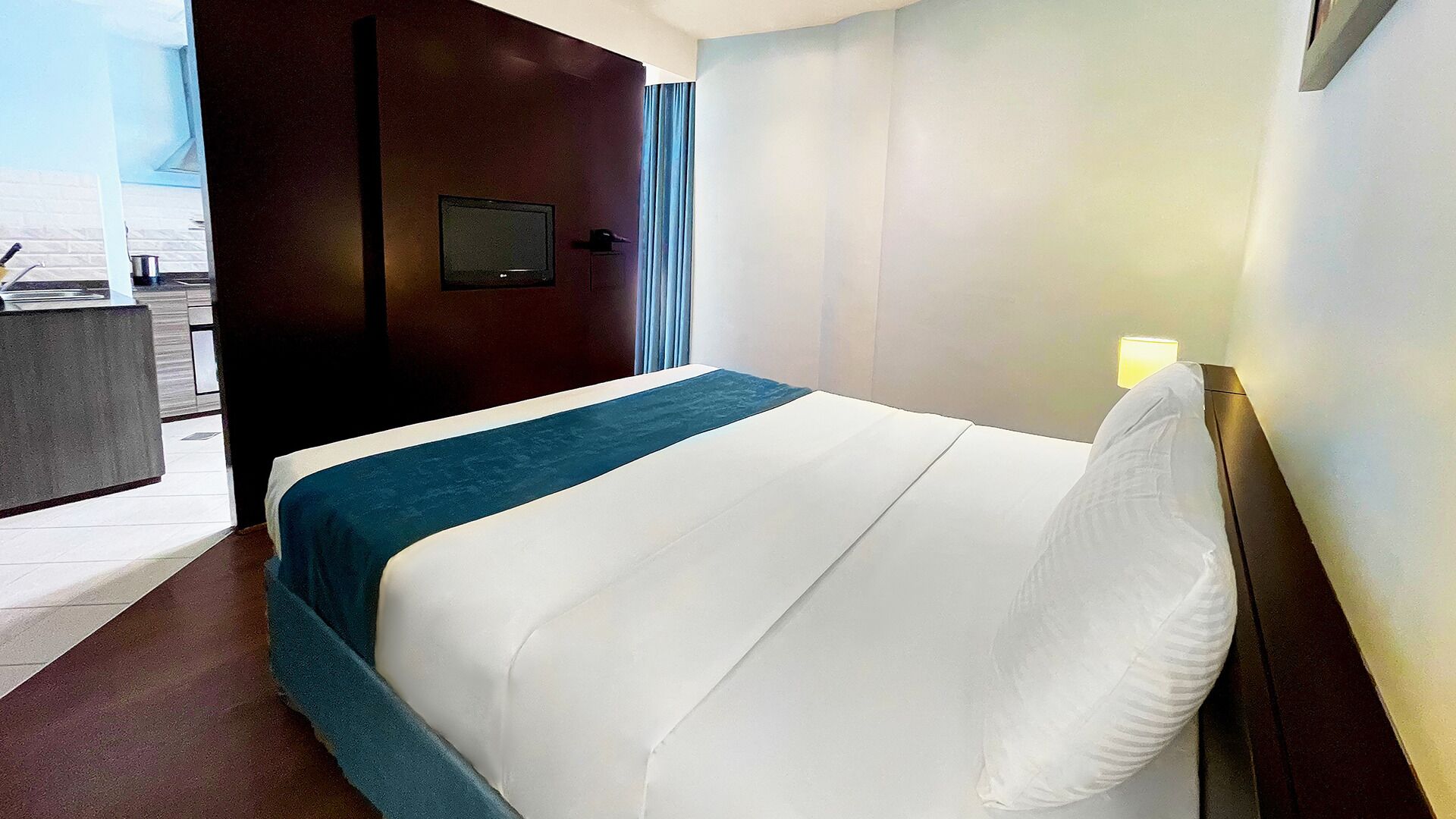 A hotel room with a bed, a TV, and a view of the outside.