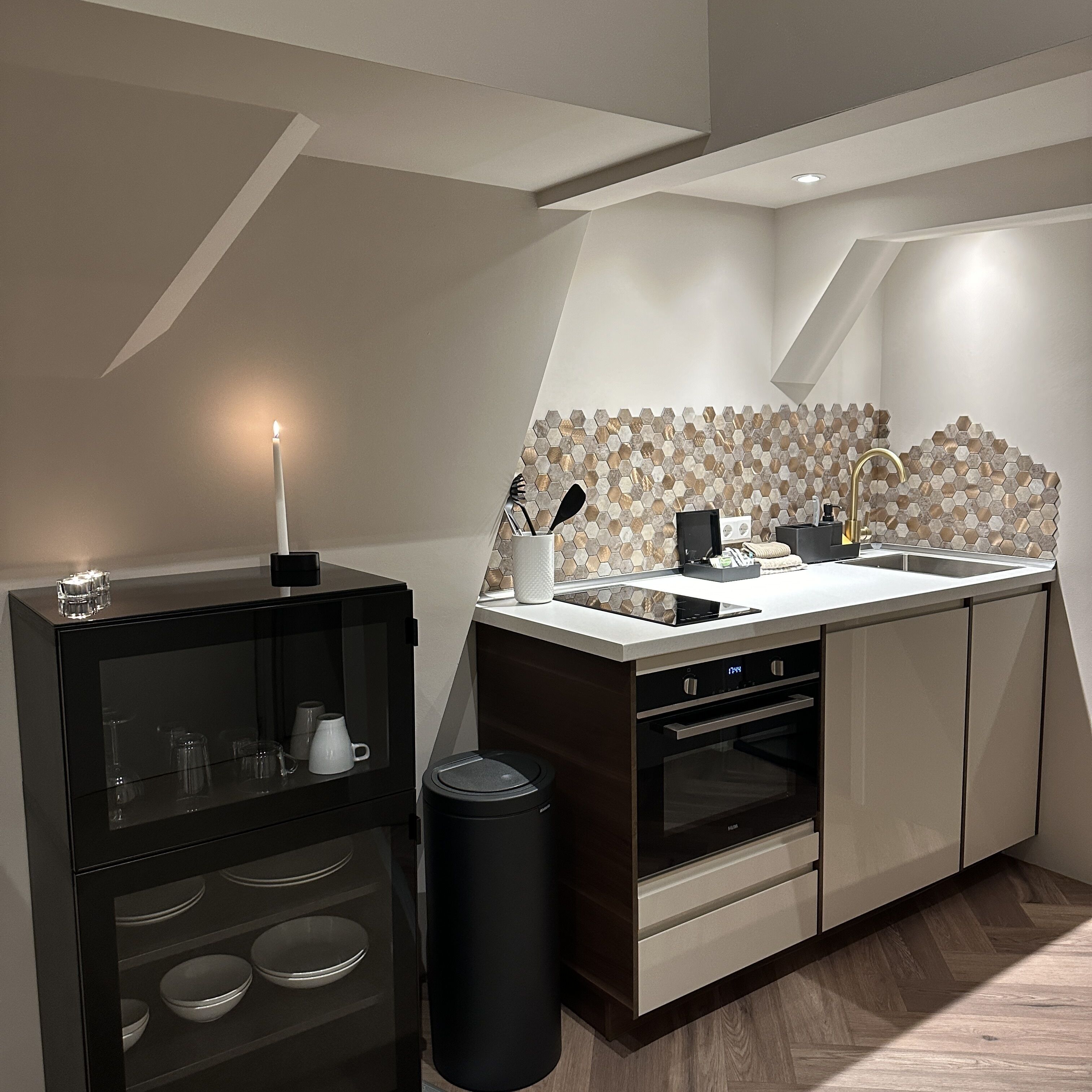 A modern kitchen with a built-in oven, a sink with a gold faucet, and a hexagonal tile backsplash.