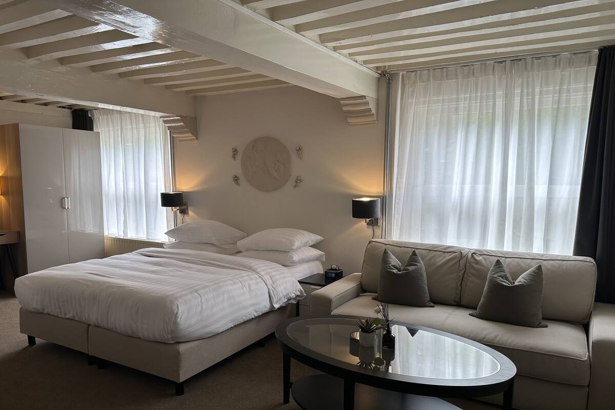 A hotel room with a bed, a sofa, a round table, and a wall clock.