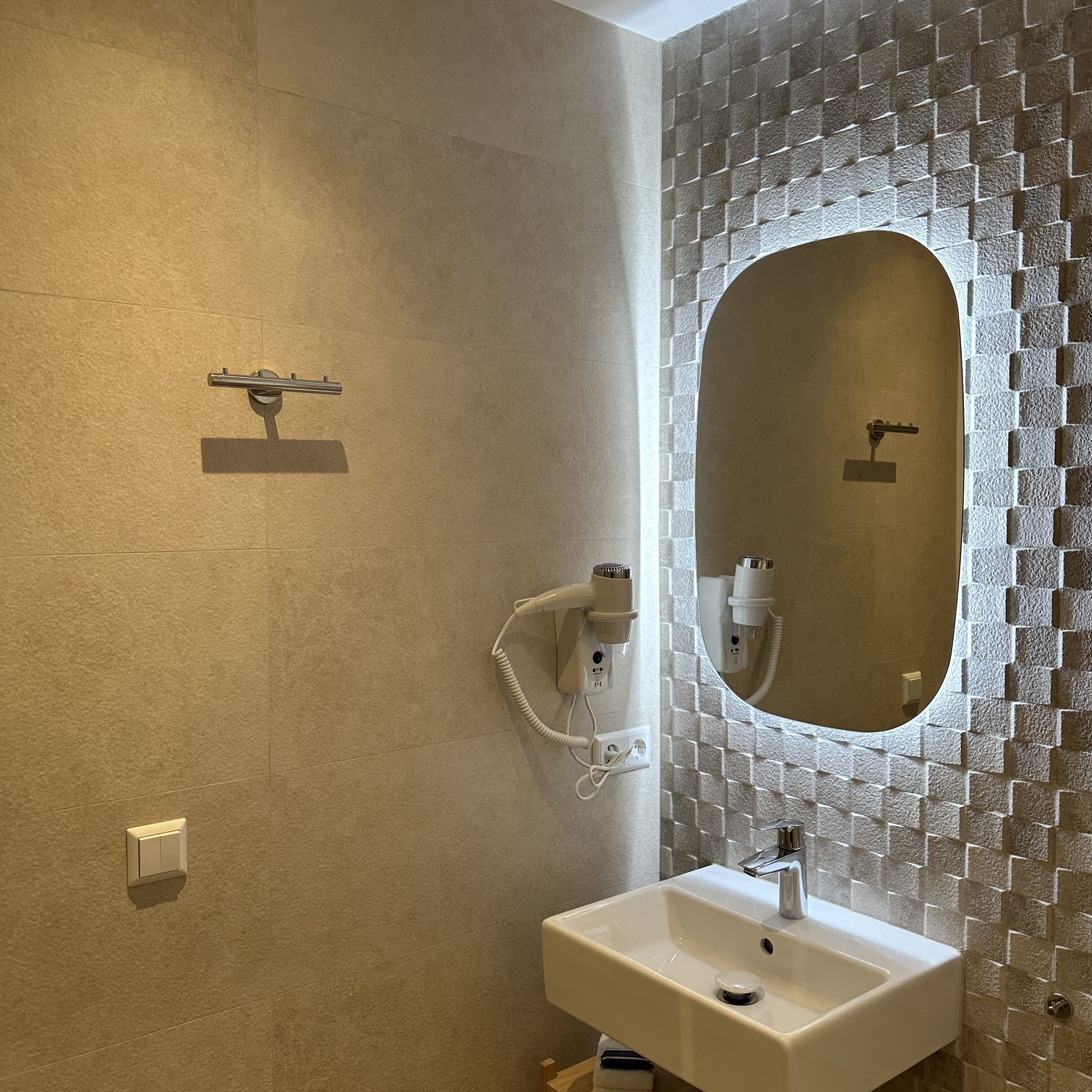 Une salle de bain avec un grand miroir, un lavabo et un sèche-cheveux fixé au mur.