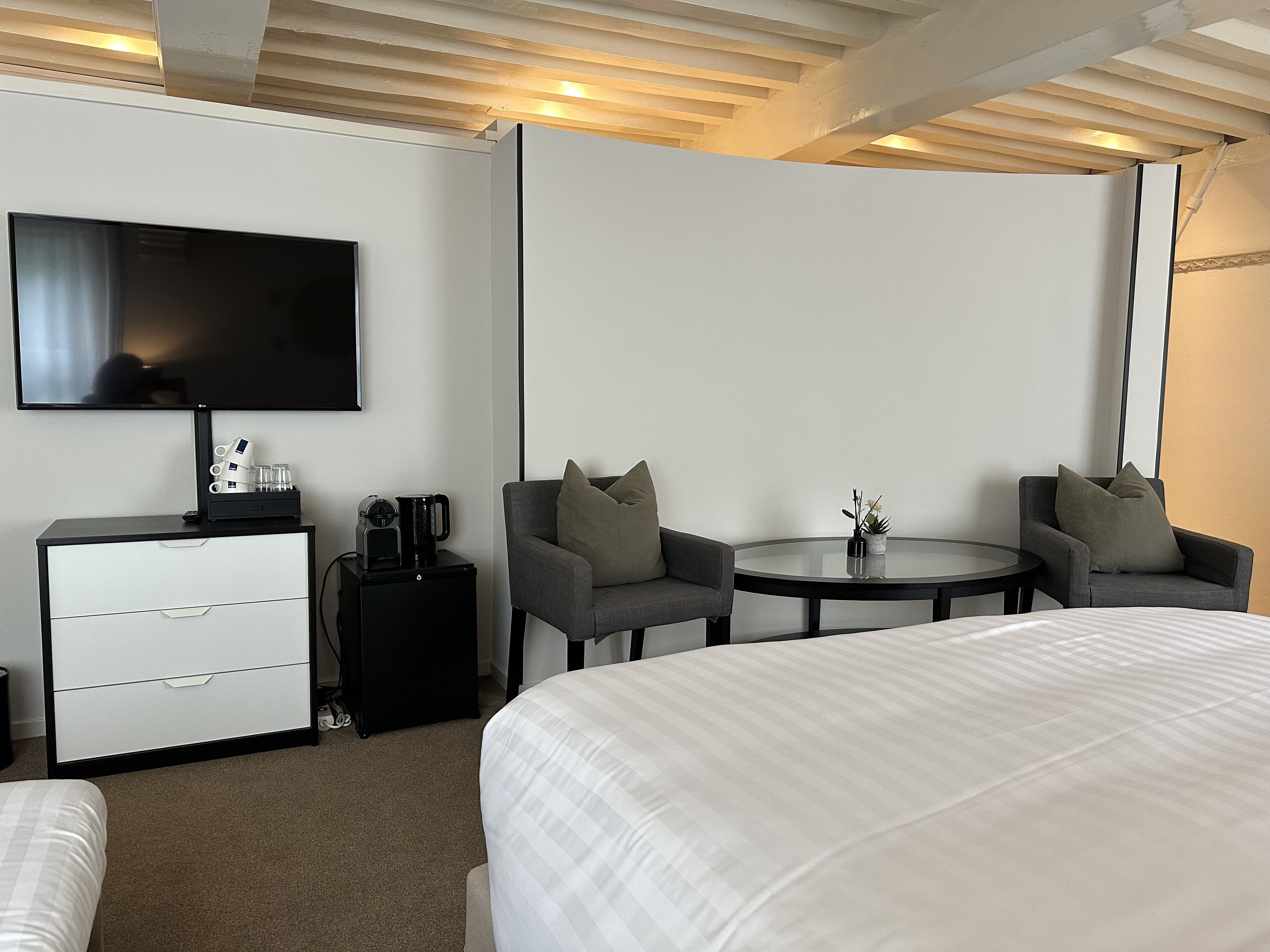 Camera d'albergo con un letto, due poltrone, un tavolino, una televisione, una macchina per il caffè e un comò.