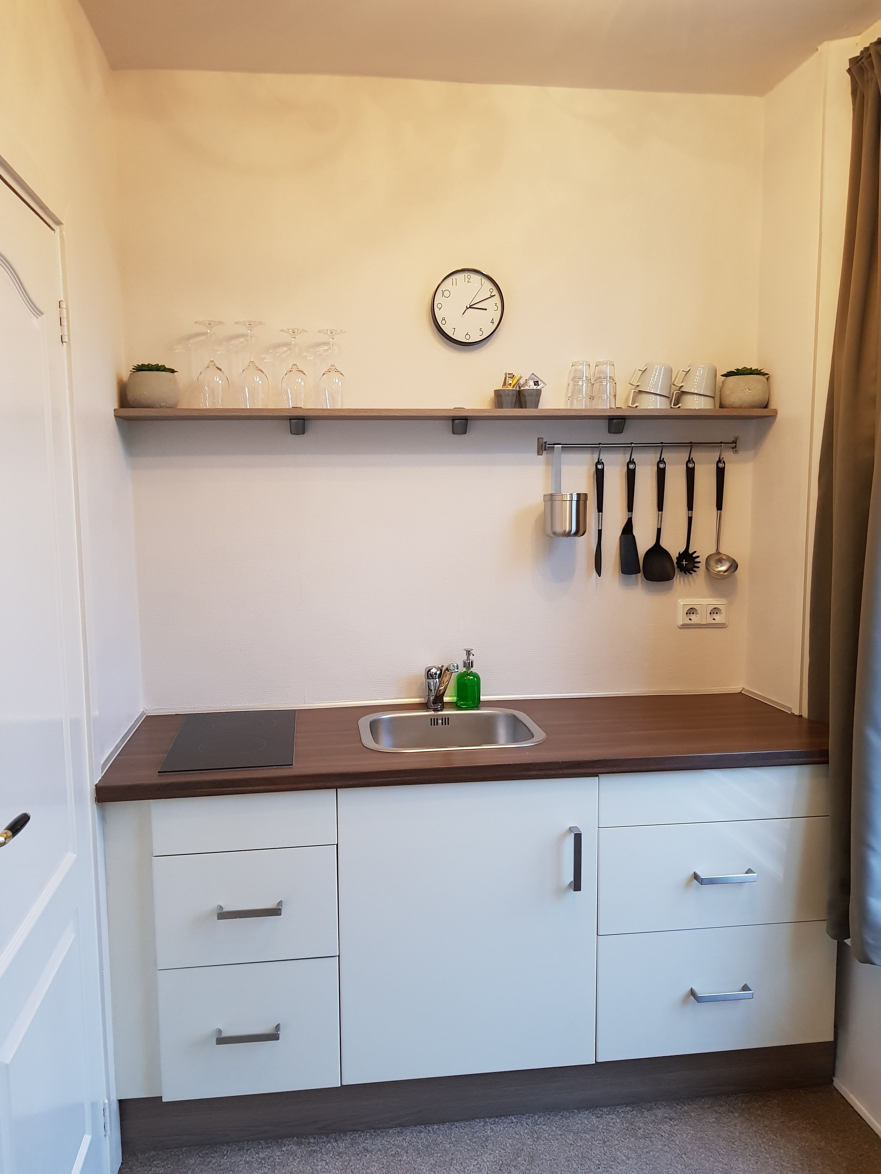 Una cocina pequeña con un lavamanos, un reloj y utensilios colgando en la pared.