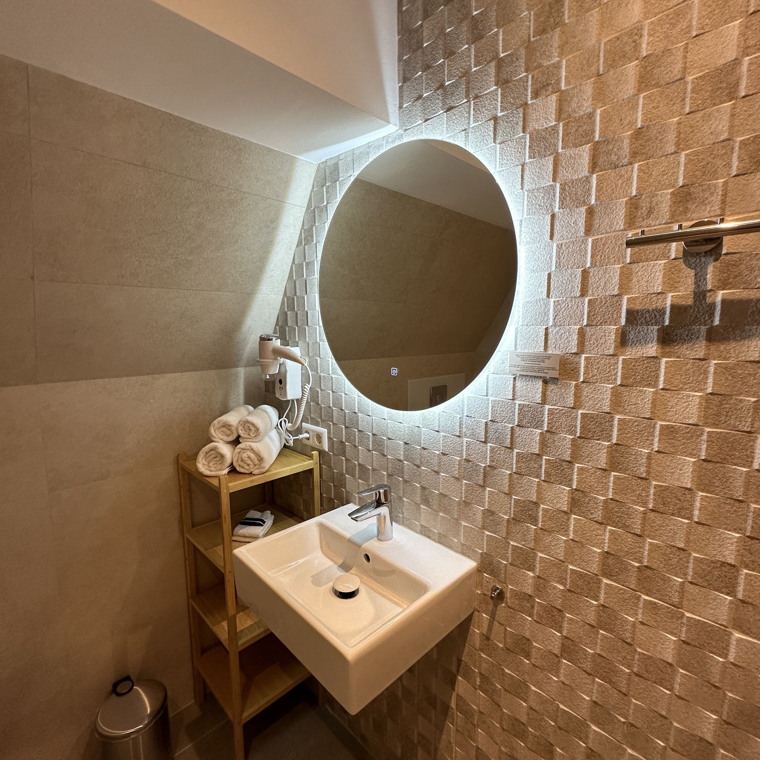 Un baño con lavamanos blanco, espejo y toallero.