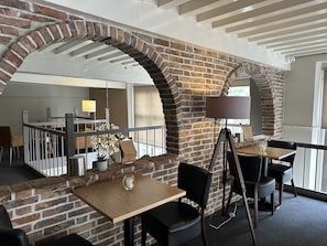A restaurant with brick walls, wooden tables, and black chairs. - Hotel Grand Canal (Delft)