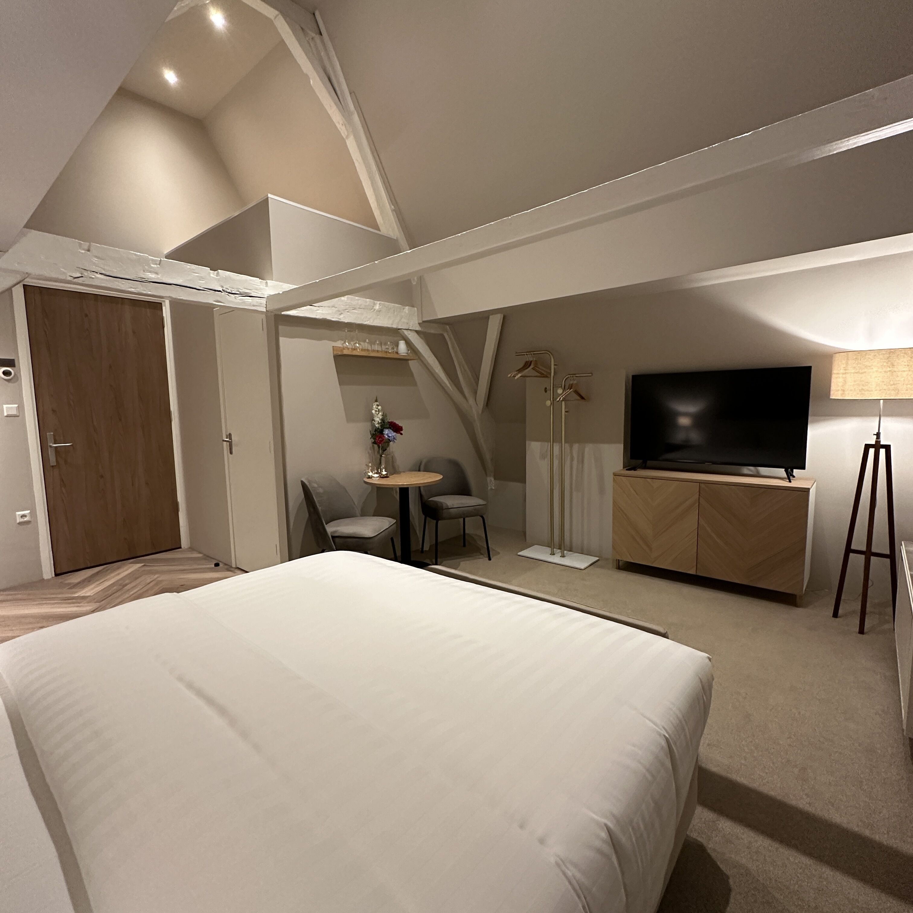Una habitación de hotel moderna con una cama grande, un televisor, un escritorio con una silla y una mesita con un jarrón de flores.