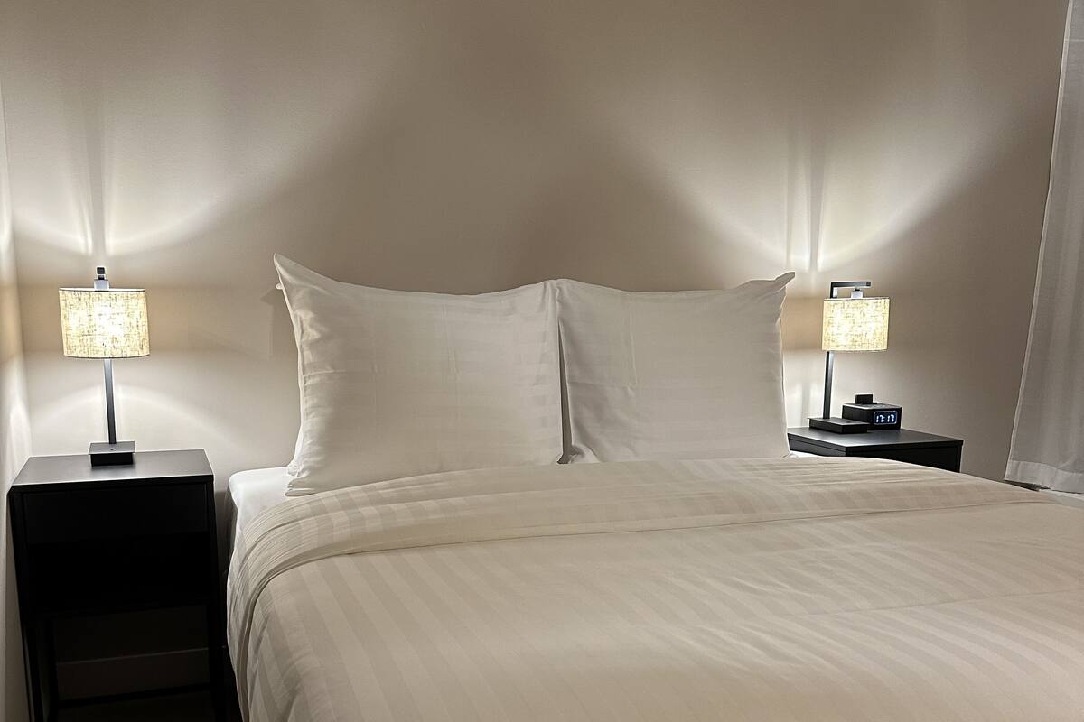 A neatly made bed with a white duvet, two bedside tables with lamps, and a digital clock on one of the tables.