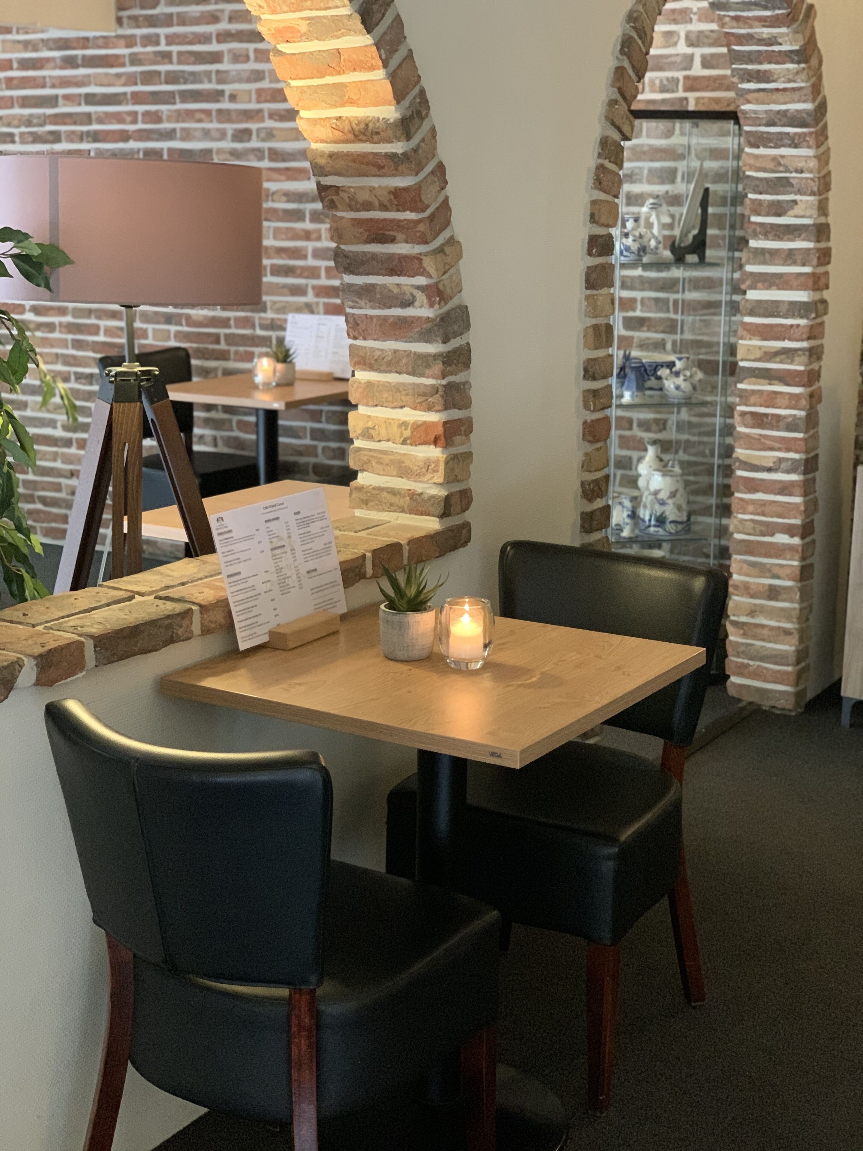 A restaurant with brick walls, wooden tables, and black chairs.