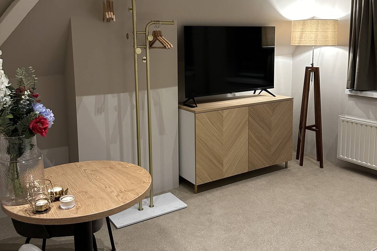A modern living room with a round wooden table, a flat-screen TV, a standing lamp, and a radiator.