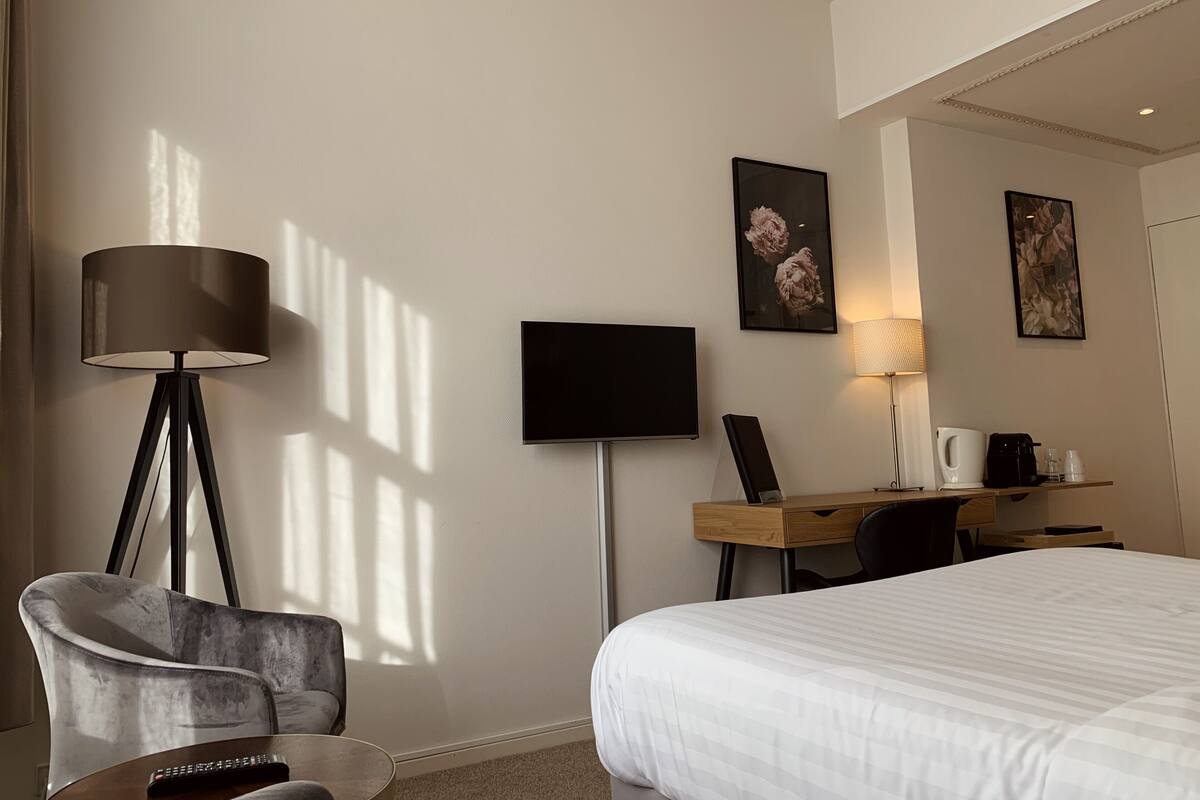 A hotel room with a bed, a desk, a chair, a TV, and a lamp.