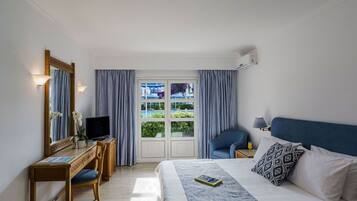Habitación de hotel con una cama, un escritorio con computadora, una silla, un televisor y una ventana con cortinas.