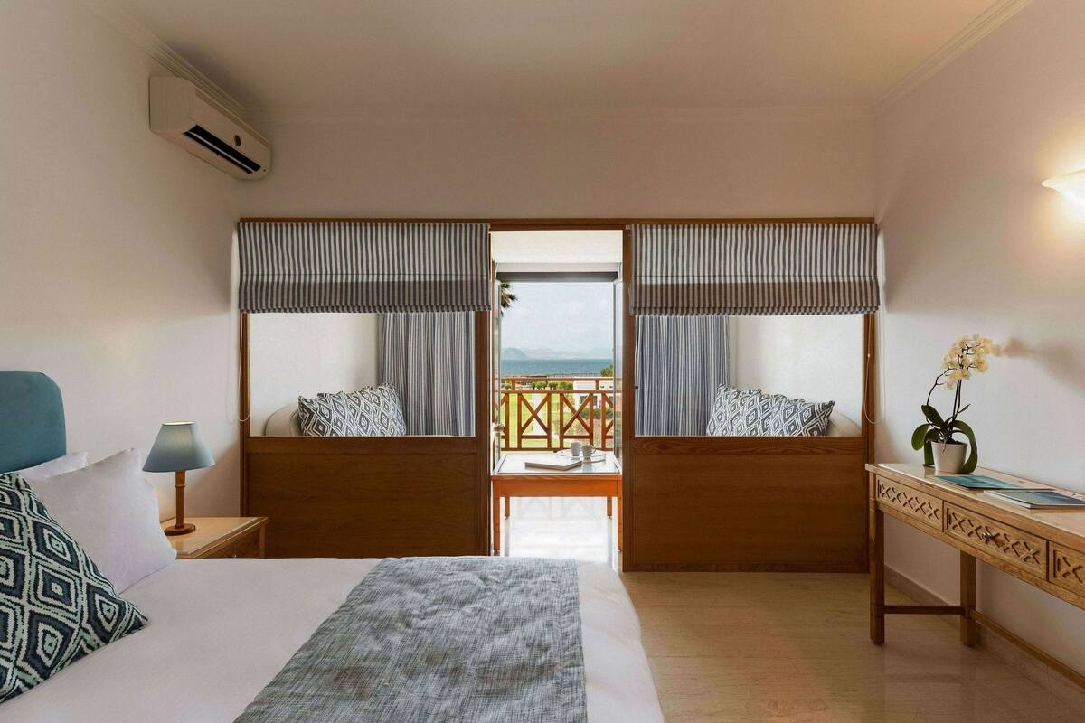 A hotel room with a bed, bedside tables, a desk, and a balcony with a view.