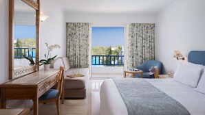 Een hotelkamer met een groot bed, een bureau, een stoel, een tafeltje en een balkon met uitzicht.