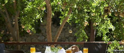 Un área de comedor al aire libre con una mesa lista para el desayuno, rodeada de abundante vegetación y árboles con frutos.