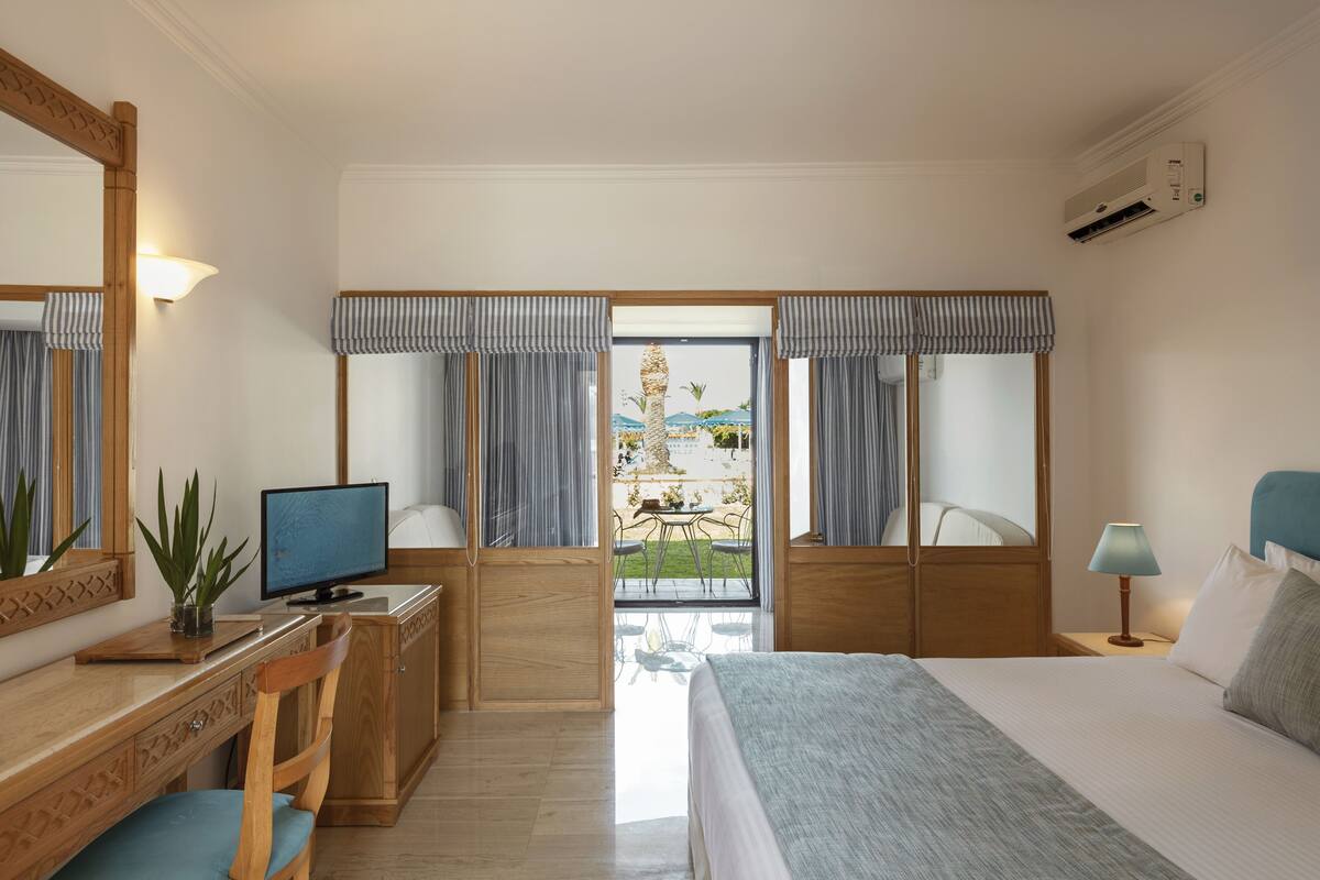 A hotel room with a bed, desk, chair, and a view of the outdoors.