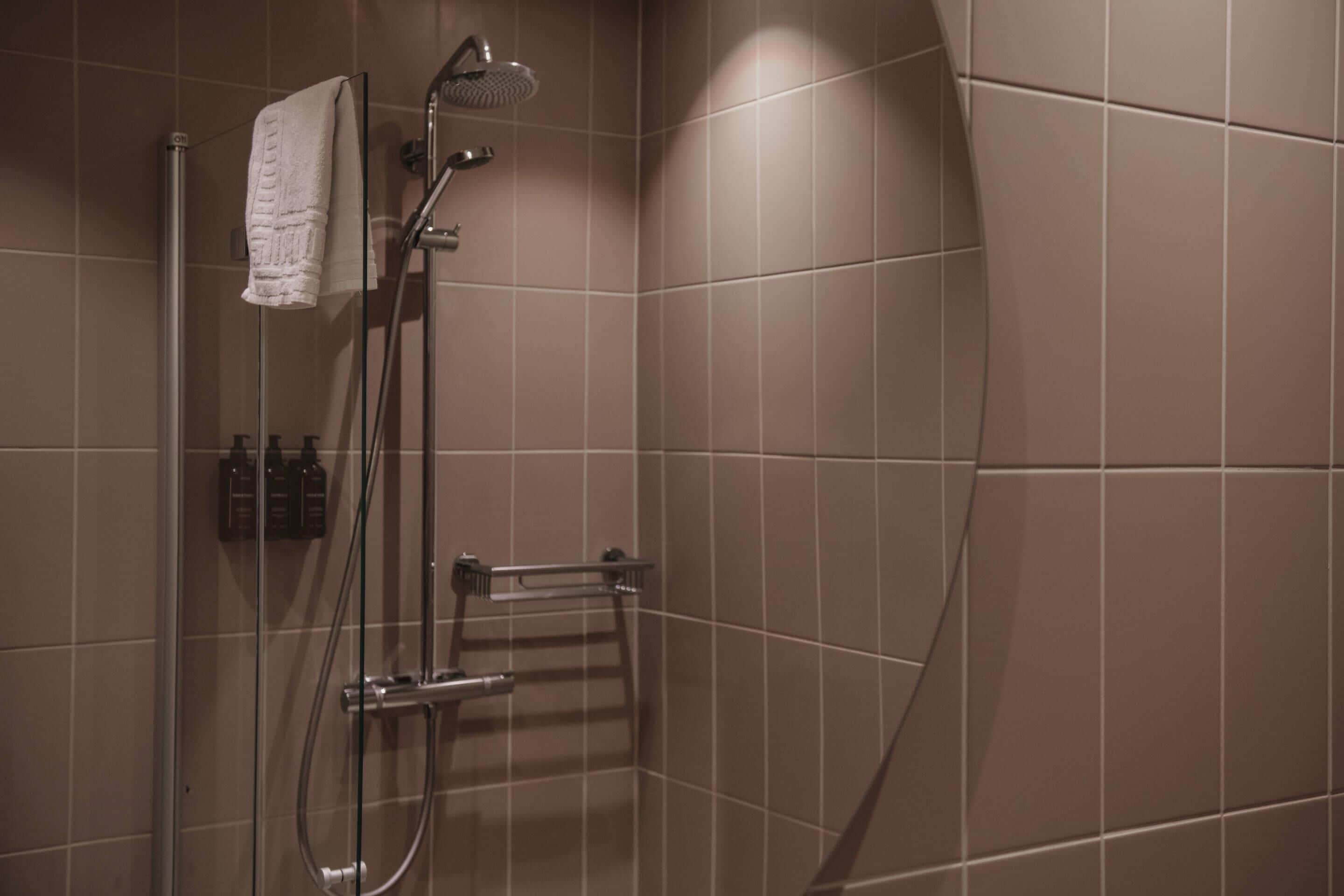 A shower with a glass door, a towel hanging on the wall, and a small shelf with toiletries.