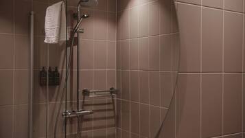 A shower with a glass door, a towel hanging on the wall, and a small shelf with toiletries.