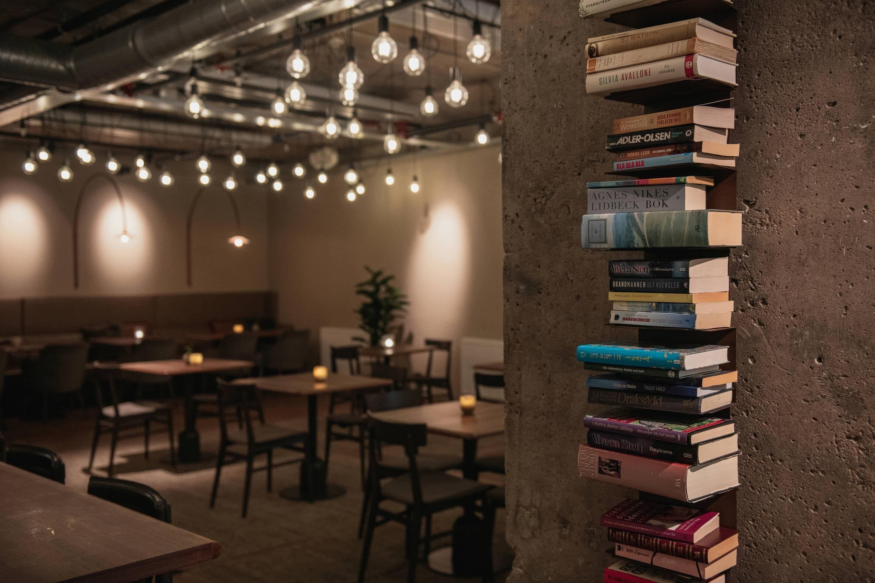Un restaurante acogedor con luces colgantes, mesas de madera y una pila de libros sobre un pilar.