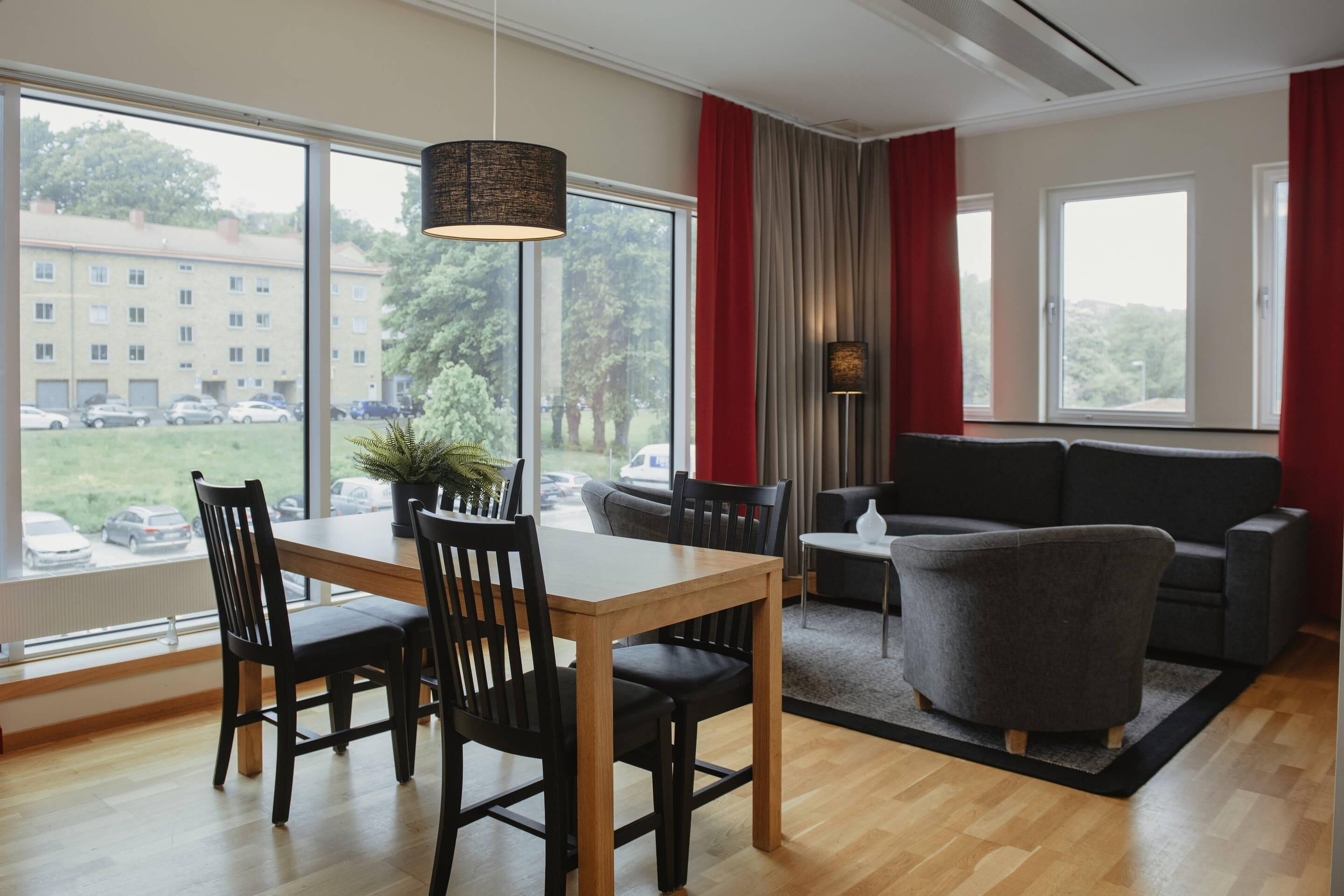 A modern living room with a dining table, chairs, a sofa, and a large window offering a view of a building and parked cars.