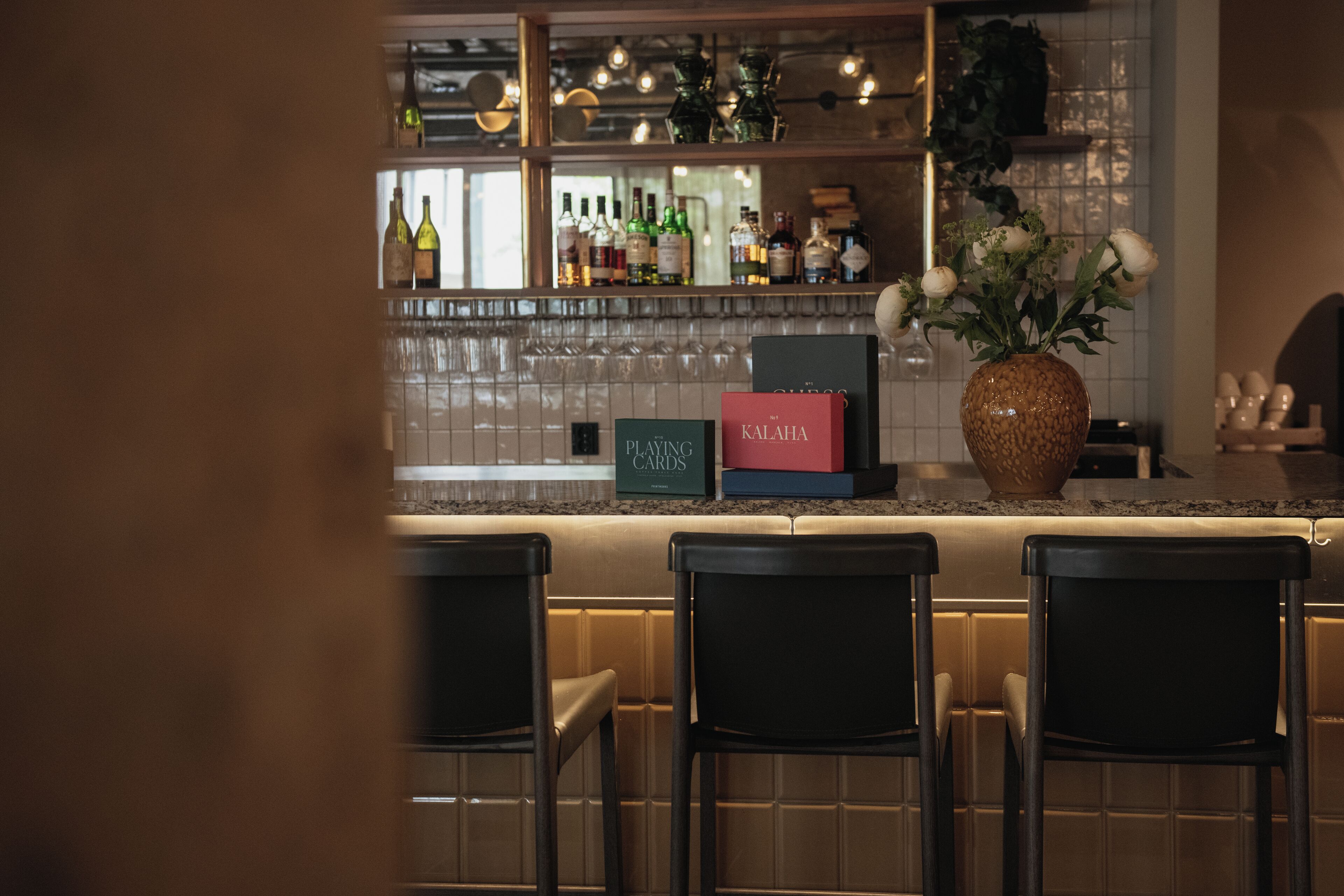 A bar area with a counter, bar stools, and a selection of bottles and glasses.