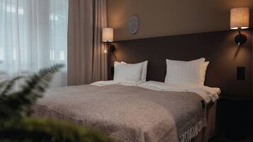 A hotel room with a large bed, two wall-mounted lamps, and a window with curtains.