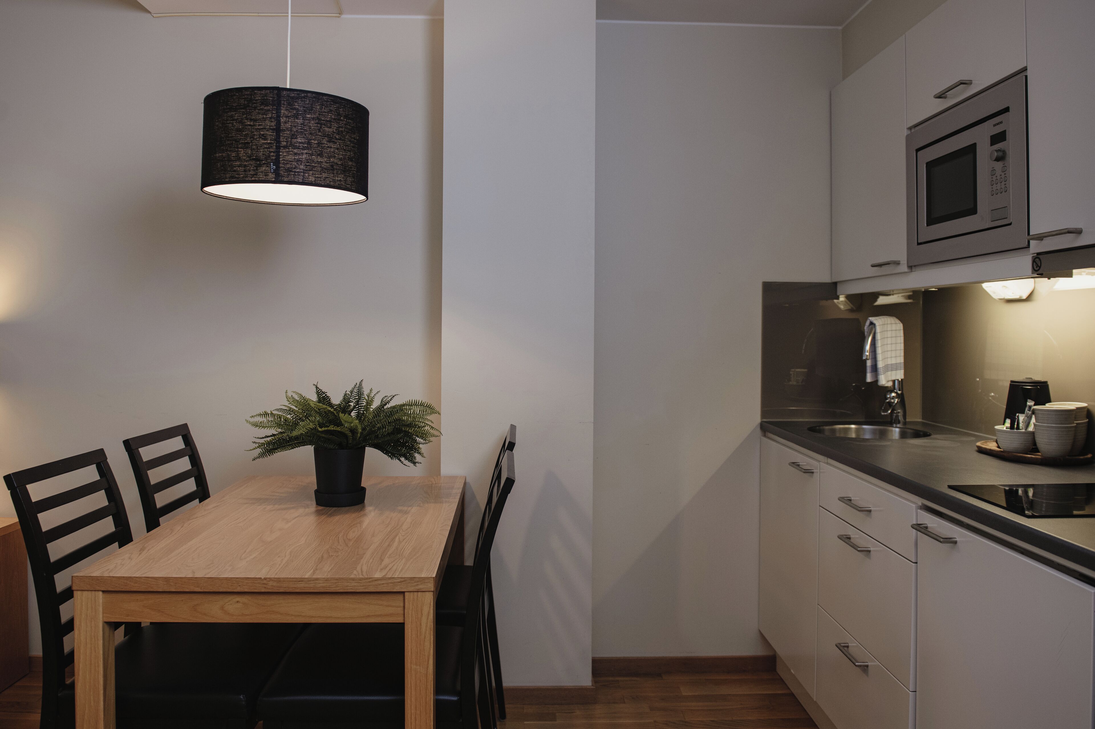 Cozinha moderna com mesa de jantar, cadeiras, luminária pendente, micro-ondas e pia.