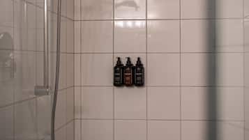 A tiled bathroom with a shower, a glass door, and three bottles of shampoo, conditioner, and body wash on the wall.
